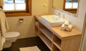 A modern bathroom with a wooden sink and a large mirror. The windows offer a view outside and the space is bright and welcoming.