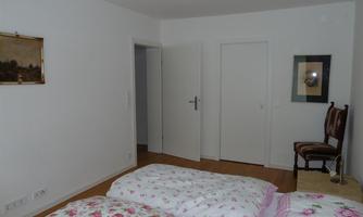 A bright bedroom with two beds and colorful bedding. A picture hangs on the wall, and a chair is next to a nightstand.