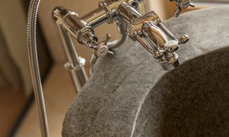 An elegant stone bathtub with a modern faucet. The silver faucet has several control valves.