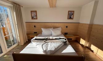 A cozy bedroom with a large bed and wooden furniture. Large windows provide plenty of natural light.