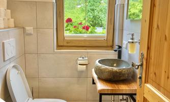 A modern bathroom with an elegant washbasin on a wooden table. Through the window, you can see mountains and green plants.