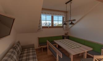 A cozy dining area with a large table and a bench. The windows offer a view of the mountains.