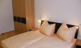 A cozy bedroom with a large bed and comfortable pillows. The room features a wooden wardrobe and a warm, inviting atmosphere.