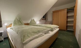 A cozy bedroom with two beds and green cushions. The room has a wooden wardrobe and soft lighting.
