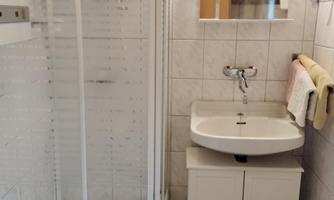 A modern bathroom with a shower and a sink. The walls are tiled in light colors and there is a small window.