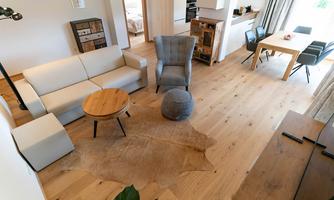 A modern living room with a bright wooden floor. There is a comfortable sofa, a coffee table, and a dining table with chairs.