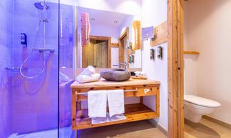 A modern bathroom with a glass shower and wooden elements. Fresh towels and a decorative stone lie on a wooden shelf.