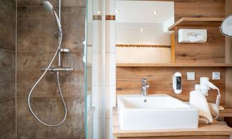 The image shows a modern bathroom with a glass shower and a sink made of white ceramic. The wooden surfaces give the room a warm and inviting ambiance.
