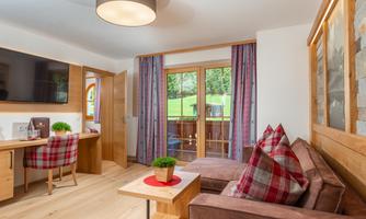 A cozy living and dining room with wood decor and modern furniture. Large windows provide a view of the greenery.