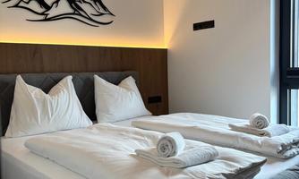 A modern bedroom with two beds and white bedding. A stylized mountain landscape hangs on the wall.