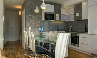 A modern kitchen with an elegant dining table and stylish chairs. The walls are decorated with appealing wallpaper, and the appliances are contemporary.