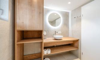 A modern bathroom with wooden shelves and a round mirror. The walls are bright, and there are placed toiletries on the table.