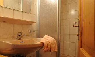 A small bathroom with a shower and a sink. The walls are tiled and there are towels in soft colors.