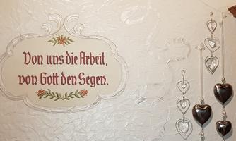A wall with a decorative saying that states: "Our work, God's blessing." Next to it, several silver heart pendants are hanging.
