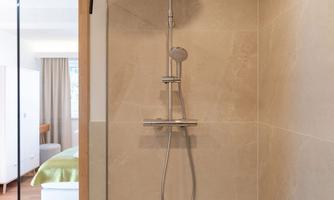 A modern shower with a large rainfall showerhead and minimalist design. The space is bright and well-designed, with a clean, elegant appearance.