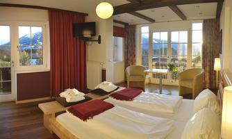 A cozy hotel room with two beds and natural light. The view from the window shows a beautiful mountain landscape.