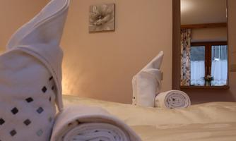 A cozy bedroom with freshly rolled towels on the bed. In the background, there is a mirror and soft lighting.