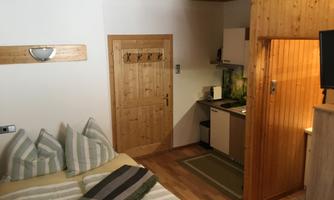 A cozy room with a double bed and a small kitchenette. Wooden paneling and bright colors create an inviting atmosphere.