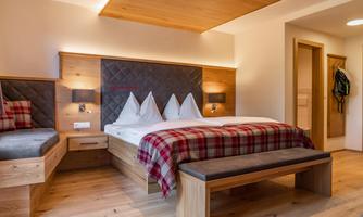 A modern bedroom with a double bed and a cozy seating area. Wooden details and a warm color scheme create an inviting atmosphere.