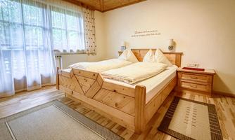 A cozy bedroom with a wooden bed and light curtains. The floor is made of wood, and there are two rugs in the room.