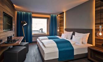 A modern hotel room with a large window and a cozy atmosphere. The furnishings include a double bed, a workspace, and stylish lighting.