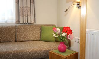 A cozy seating area with a gray sofa and colorful cushions. On a small table, there is a vase with fresh flowers.