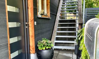 An inviting entrance area with a modern front door and a staircase. A flower pot stands next to the door on a paved floor.