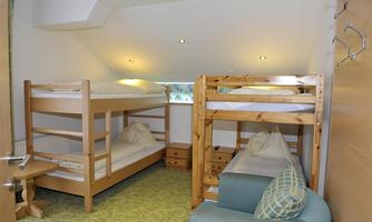 A simple bedroom with a bunk bed and a single bed. The room has a modern look with wooden details and a cozy armchair.