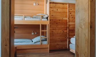 A cozy room with a wooden bunk bed and separate sleeping accommodations. The walls are also made of wood, giving the space a warm atmosphere.