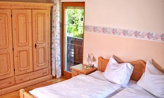 A cozy bedroom with a wooden wardrobe and a large bed. The window offers a view of the outdoor area.