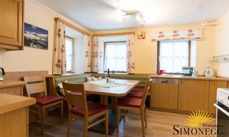 A cozy kitchen with a large dining table and wooden cabinets. Bright colors and windows create an inviting atmosphere.