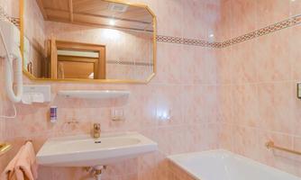 A modern bathroom with a bathtub and a sink. The walls are painted in soft shades of pink, and wooden details add warmth.