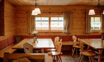 A cozy room with wooden paneling and several tables. The window lets in plenty of daylight and there are decorative curtains.