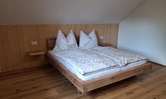 A cozy bedroom with a wood-colored bed. The walls are made of wood, and there are two large pillows on the bed.