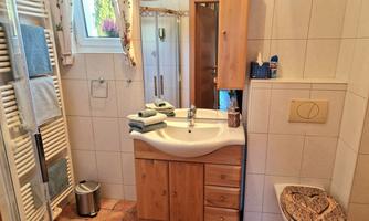 A modern bathroom with wooden cabinets and tiles. It includes a shower, a sink, and a toilet.