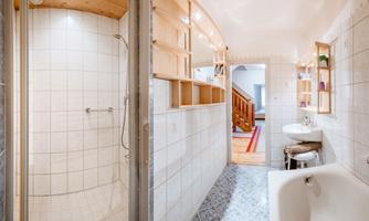 A modern bathroom with a shower and a bathtub. Bright tiles and wooden shelves create a cheerful atmosphere.