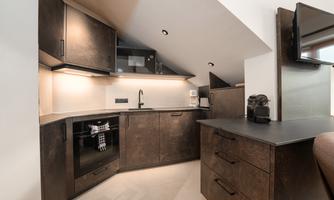 A modern kitchen in the attic with dark wood cabinets and elegant surfaces. The lighting creates a bright and inviting atmosphere.