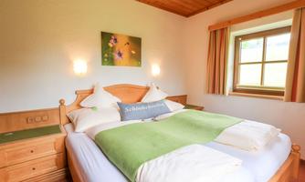 A cozy bedroom with two single beds and light wooden furniture. The room has large windows that let in natural light.