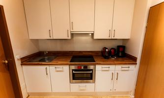 A modern kitchen with white cabinets and a wooden countertop. There is a stove, an oven, and kitchen appliances on the counter.