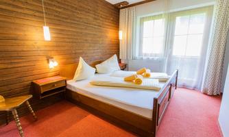 A cozy bedroom with wooden walls and a large double bed. Yellow towels are on the bed, and the room has plenty of natural light.