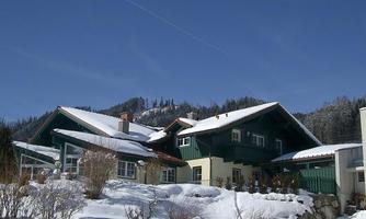 A beautiful two-story house in the snow, surrounded by snow-covered trees. The clear blue sky contrasts with the wintry landscape.
