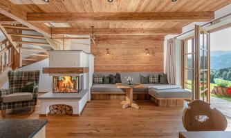 A cozy living room with a wooden ceiling and a warm fireplace. Large windows provide a view of the mountains.