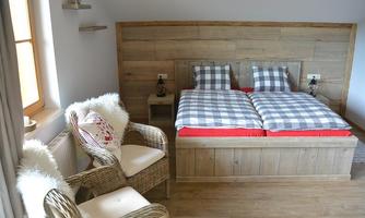 A cozy bedroom with a double bed and checkered bedspreads. Two wicker armchairs blend into the rustic decor.