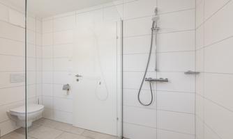 A modern bathroom with a glass shower and white tiles. The toilet is stylish and simply designed.