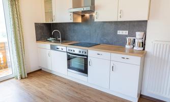 A modern kitchen with white cabinets and a wooden countertop. It is well equipped with a stove, a sink, and a coffee machine.
