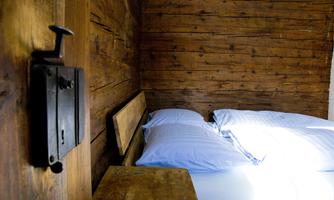 A cozy room with wooden walls and a bed with blue pillows. A vintage lock is visible on the wall.