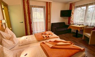 A cozy room with two beds and orange blankets. There is a table, a chair, and a window with a view outside.