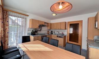 A modern kitchen with a large table and black chairs. The wooden furniture and the daylight create an inviting atmosphere.