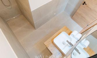 A modern bathroom with a large shower and an elegant sink arrangement. The walls are in neutral tones, and the wooden details add warmth.