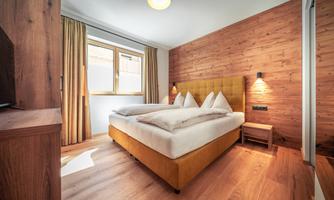 A modern bedroom with a comfortable double bed and wood paneling. Large windows provide plenty of daylight and a cozy atmosphere.